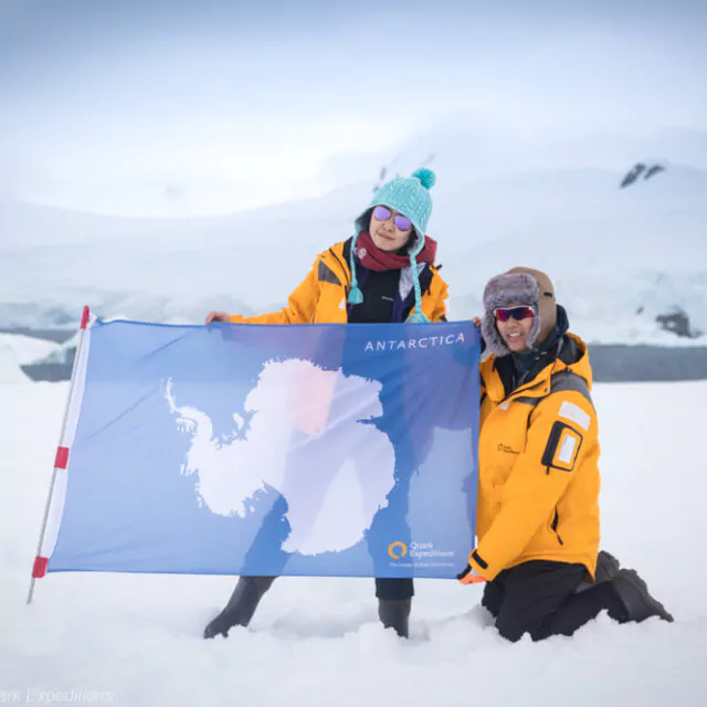 Zwei Passagiere mit einer Flagge der Antarktis auf dem Kontinent.