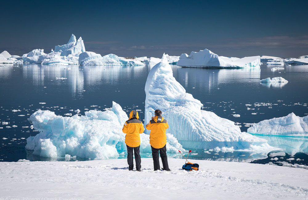 Zwei Passagiere in der Antarktis mit Blick auf das Eismeer und Eisberge vom Land