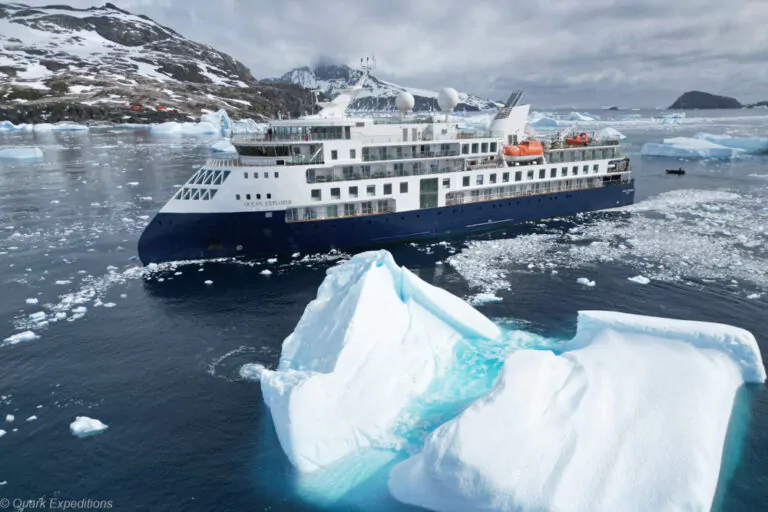 Schiff Ocean Explorer von Quark Expeditions in der Antarktis mit einem Eisberg im Vordergrund.